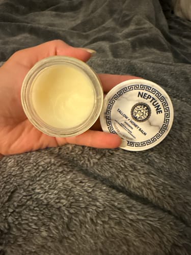Customer holds an open jar of the Grass Fed Tallow & Honey Balm, showing its creamy, light-yellow texture.