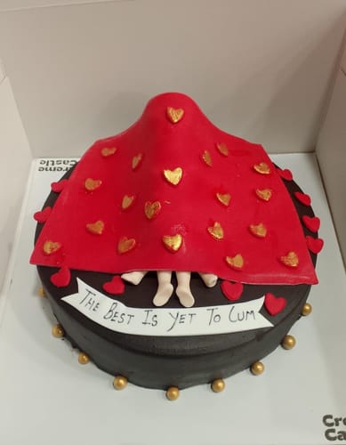 Customer's Naughty under Blanket Cake, showing fondant feet peeking from under a red blanket on a dark brown cake base.