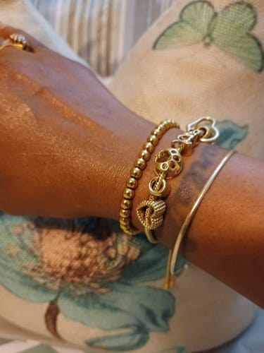 Reviewer's wrist wearing the gold Caicos Beaded Bracelet stacked with two other bracelets against a floral background.
