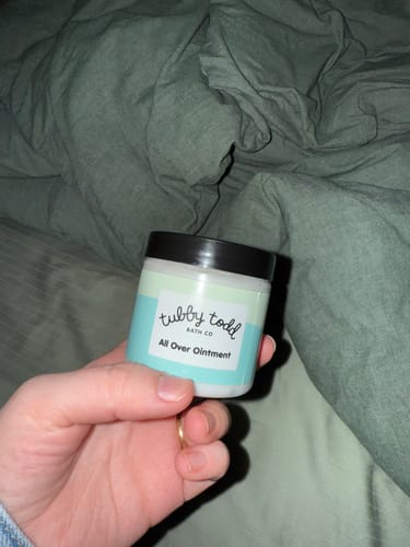 Customer holding a small tub of Tubby Todd All Over Ointment in their hand.