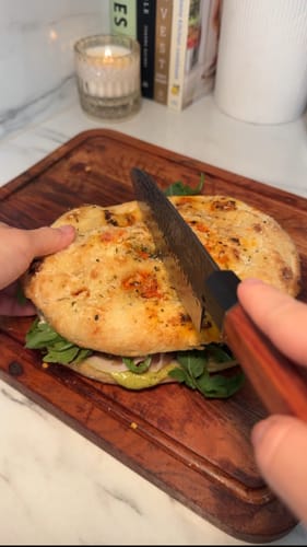 Reviewer slicing a large sandwich with the sharp Gyuto Japanese Chef Knife on a cutting board.