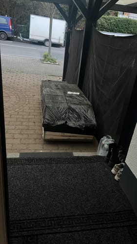 Kunde zeigt die Verpackung der SWAT Multipresse, die in schwarzer Folie auf einer Palette vor der Tür geliefert wurde.