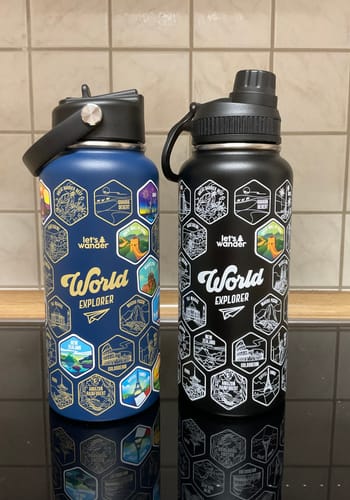 Customer's blue and black World Explorer Bottles on a counter. The blue bottle is decorated with colorful destination stickers.