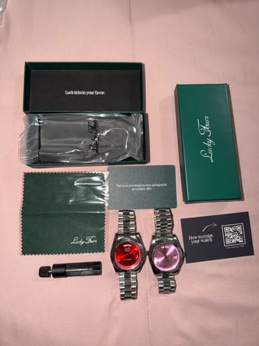 Customer's two Lucky Fours® Santos watches, one with a red dial and one pink, shown with their green boxes and accessories.