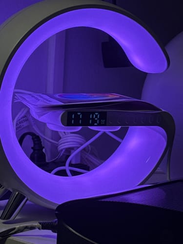 Customer's LitLamp™ alarm clock glowing with a purple light, with the digital clock showing 17:19 and a phone on the charger.