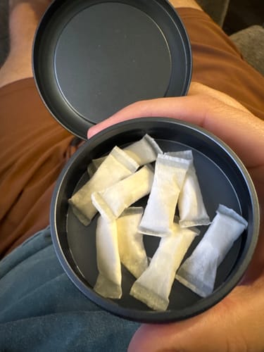 Customer holding an open dark tin filled with several Mountain Wintergreen Nicotine Pouches.