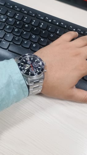 Reseñador muestra su reloj Orient Mako Chronograph con correa metálica y esfera negra en la muñeca junto a un teclado.