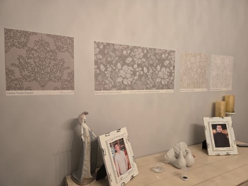 Customer comparing a gray Bates Wallpaper sample against other samples on a wall.