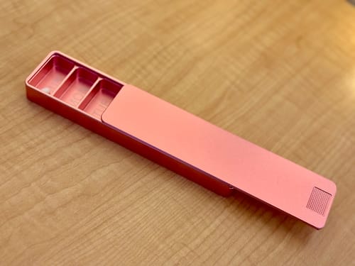 Customer's pink aluminum Weekly Case partially open on a wooden table, showing the pill compartments inside.
