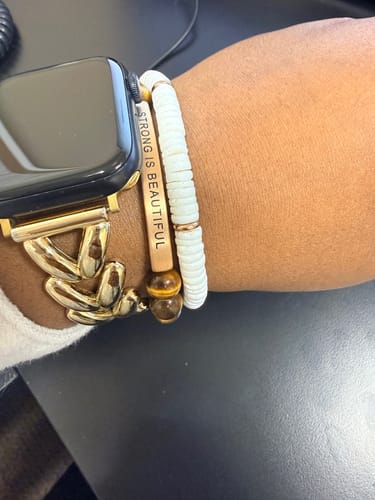 Customer wearing the white Puka Shells accent bracelet stacked with an engraved bracelet and watch on their wrist.