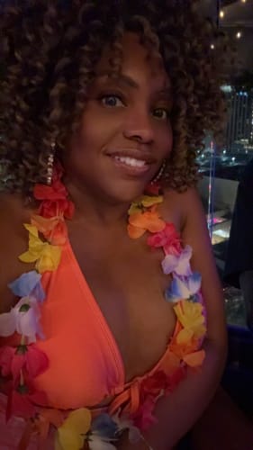 Reviewer smiling at night wearing a lei, showing off her curly, highlighted Freetress Wand Curl Crochet Braid.