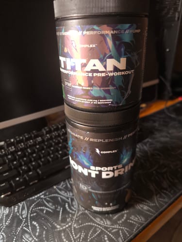 Reviewer's Titan Pre-workout tub stacked on top of another supplement container on a desk.