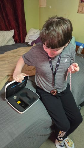 Customer's photo of a child looking into the open case for the Qi Coil™ Mini System, wearing the coil.