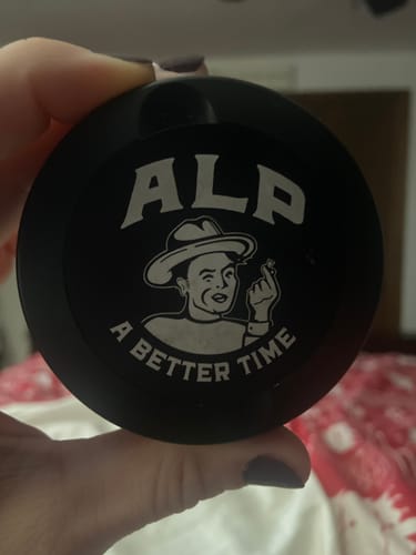 Reviewer holding a round, black container of ALP Nicotine Pouches, showing the logo.