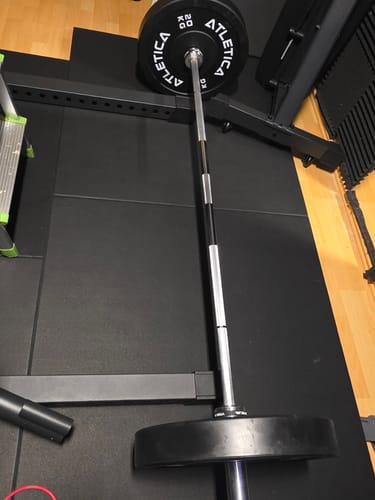 Die stabile Alpha Langhantel eines Kunden, beladen mit Hantelscheiben, auf einem Fitnessboden.