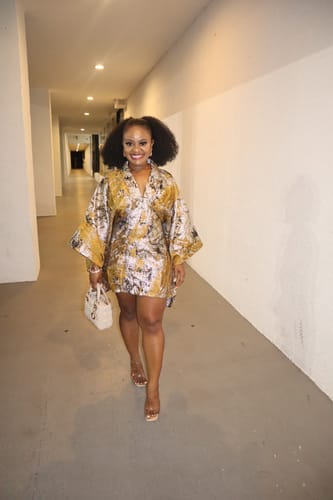 Reviewer smiling and walking down a hallway, wearing the Sensationnel Textured Drawstring Ponytail in a high, full style.