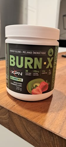 Photo d'un client montrant le pot de Burn-X saveur Fraise & Kiwi, posé sur une surface en bois.