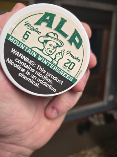 Close-up of a customer holding the white tin of Mountain Wintergreen Nicotine Pouches.