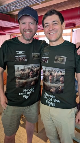 Two customers showing off their matching dark green unisex t-shirts with a large graphic print.
