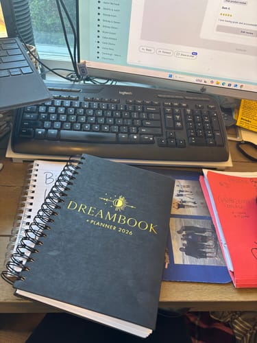 A customer's 2026 Dreambook + Planner with a dark, spiral-bound cover, shown on a desk.
