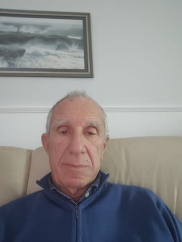 Un cliente anziano si fa un selfie seduto su un divano beige in casa.