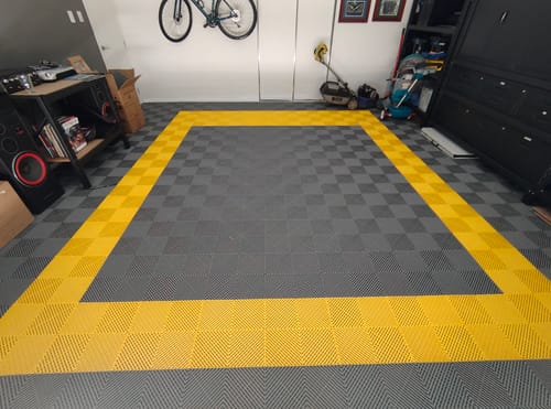 Customer's garage floor with newly installed modular tiles in a stylish yellow border and dark grey checkered pattern.