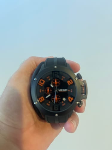 Customer's hand holding a black Lucky Fours® Chronograph watch with bold orange accents.