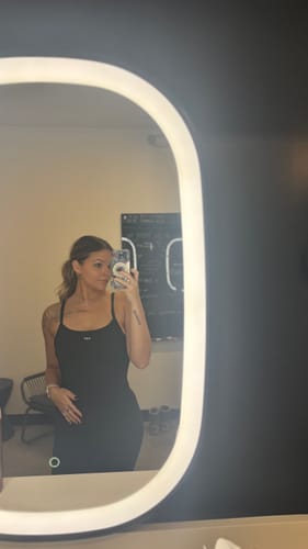 Customer's mirror selfie showing the top of the sleek, black Flare Onesie and its adjustable straps.
