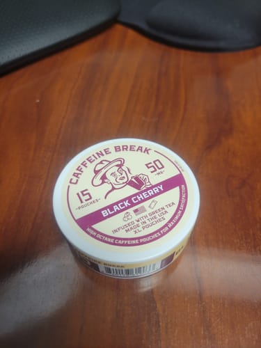 Customer's round tin of Caffeine Break Black Cherry Caffeine Pouches sitting on a wooden desk.