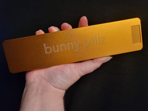 Reviewer holding the closed, gold-colored metal Weekly Case in their hand against a dark background.