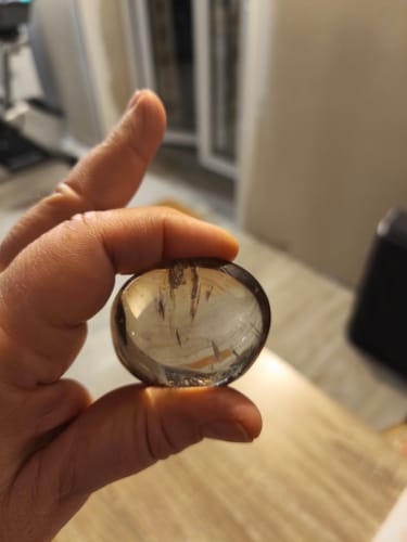 Client tenant dans sa main un galet de Quartz fumé translucide.