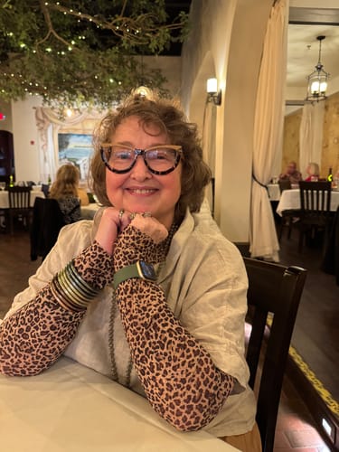 Reviewer at a table wearing the Leopard Print Mesh Top, showing the sleeves layered under a beige shirt.