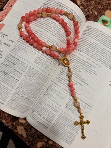 Customer's handmade pink rosary with a brass crucifix resting on an open book.