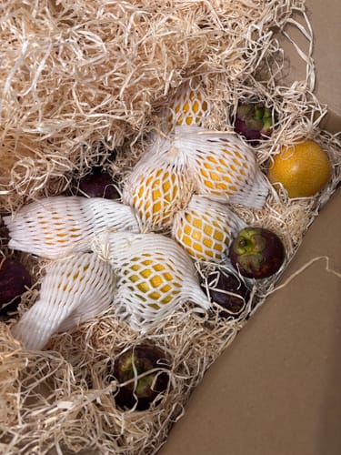 Ein Kunde zeigt die geöffnete Granadilla & Mangostan Box, in der die frischen Früchte in Holzwolle verpackt sind.