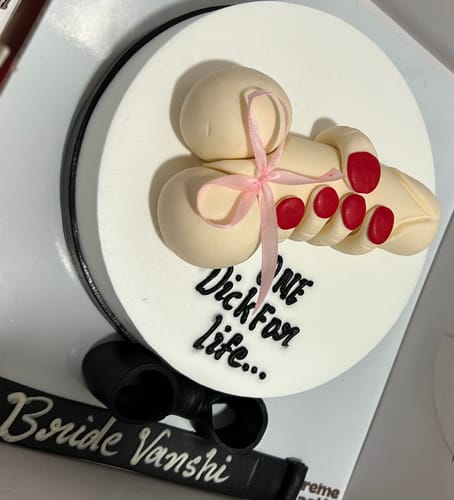Customer's white bachelorette party cake with a fondant hand holding a phallic object and text reading 'One Dick For life...'.