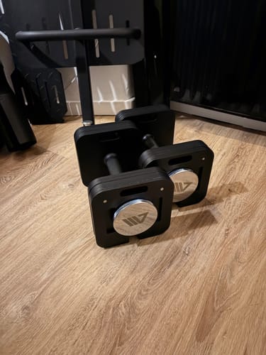 Kunde zeigt die als Ersatzteile erhaltenen schwarzen Kurzhanteln auf einem Holzboden.