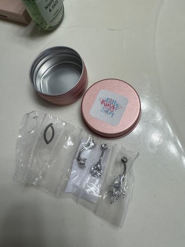 Customer's new titanium gem belly rings in sterile packaging, displayed next to their round storage tin.
