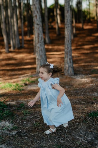 Customer's child wearing the Shine Like A Pearl Blue Smocked Dress while playing in a wooded area.