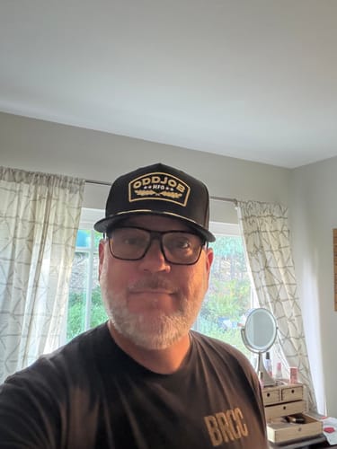Customer smiling while wearing the black Big Military Hat in a well-lit room.