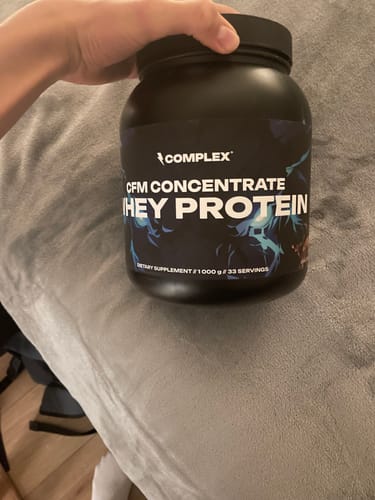 Reviewer holding a large black tub of Complex CFM Concentrate Whey Protein.