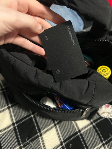 Reviewer placing the black SPOTMINDERS Tracking Card into a pocket on a black bag.