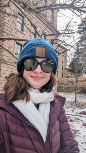 Reviewer smiling while wearing the cozy, cream Bradie Scarf with a winter coat on a cold day.