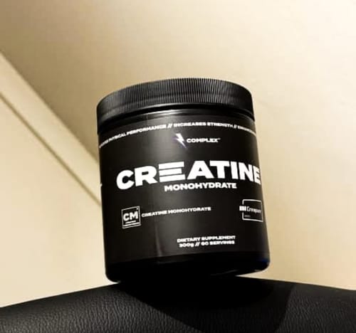 Reviewer's black tub of Complex Creapure Creatine supplement resting on a surface.