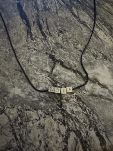 Customer's custom friendship charms with letters spelling a name on a black cord necklace.