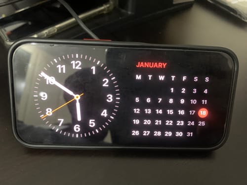 Customer's iPhone displaying a clock and calendar while charging on the SPOTMINDERS. Wireless Charger.