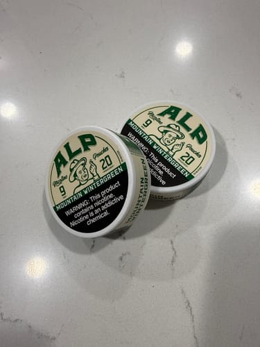 A customer's two white tins of ALP Mountain Wintergreen Nicotine Pouches on a countertop.