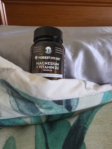 Customer's bottle of Magnesium + Vitamin D2 resting on a pillow on a bed, reinforcing the review's theme of improved sleep.