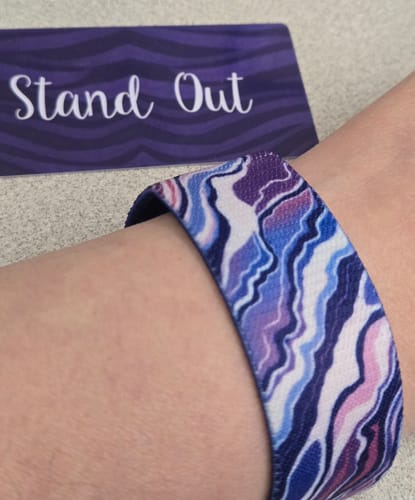 Customer wearing a colorful patterned strap from a Mystery 3-Pack with the 'Stand Out' collector card in the background.
