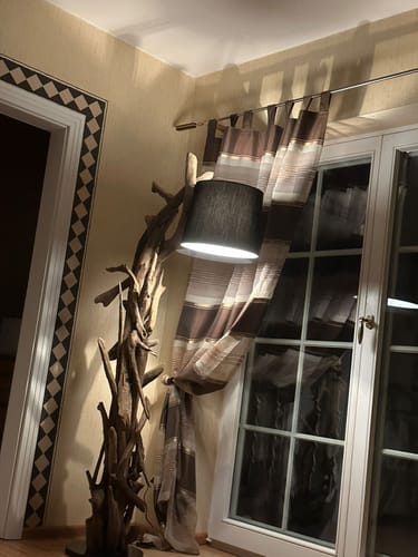 Kunde zeigt die rustikale Wurzel Holz Lampe MORGAN mit ihrem schwarzen Lampenschirm, beleuchtet in einer Ecke.