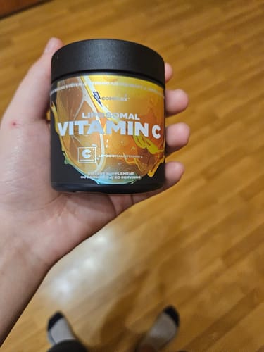 Reviewer holding a black tub of Liposomal Vitamin C.